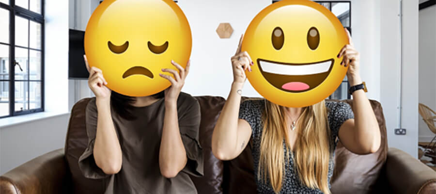 Two people holding a sad and happy emoji in front of their faces.